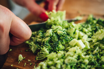 Closeup of a female chopping the fresh and tasty broccoli with a knife on a wooden cutting board