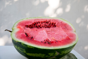 Half a red juicy watermelon on the background of a white shady wall. The concept of healthy natural food.