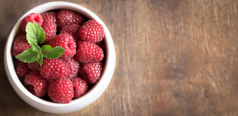 Ripe fresh raspberries in a white bowl on a brown wooden background.