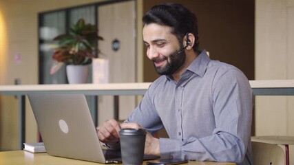 Happy indian business man customer support agent or salesman wearing headset talking, having virtual meeting working on laptop computer giving online training, remote class on video conference call.