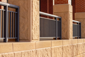 Abstract texture view of a modern beige stone and red brick urban building wall with an attractive durable metal protective fence, in bright sunlight