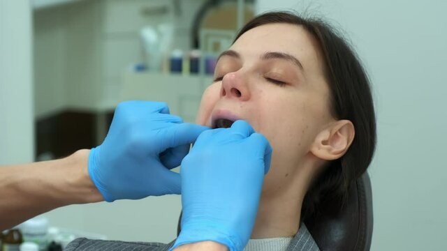 Portrait of woman in dentistry, doctor orthodontist inserts silicone teeth trainer into her mouth to correct her teeth, hands in gloves closeup. Correction of the bite and treatment of the jaw joint.