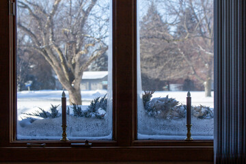 This image features an abstract texture background of an ice frosted window with holiday candlesticks on its window sill, showing an outdoor winter snow landscape view.