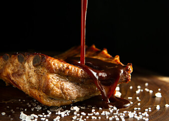 Roasted pork ribs on a wood base with salt, pouring barbecue sauce and copy space