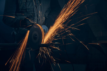 Close up of worker in special black suit working with angle grinder and grinding metal with large...