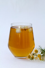 chamomile tea. glass cup of iced Herbal chamomile tea on a white table with copy space. cup of tea with fresh flowers and green leaves on white background. vertical