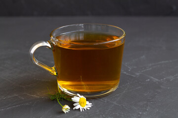 hot drinks. mug of chamomile tea. glass cup of iced Herbal chamomile tea on a black table with copy space. cup of tea with fresh flowers and green leaves on grey background.