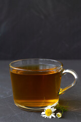 hot drinks. mug of chamomile tea. glass cup of iced Herbal chamomile tea on a black table with copy space. cup of tea with fresh flowers and green leaves on grey background.