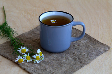 cup of tea with flowers.hot drinks. grey mug of chamomile tea on sackcloth. cup of hot Herbal chamomile tea on a wooden table with copy space with fresh flowers and green leaves on light background.