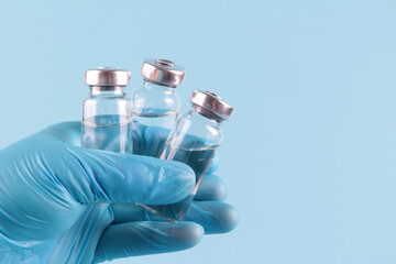 The doctor's gloved hand holds vials of medicines on a blue background. The covid-19 vaccine.The concept of prevention,immunization, vaccination and treatment of coronavirus infection.Copyspace