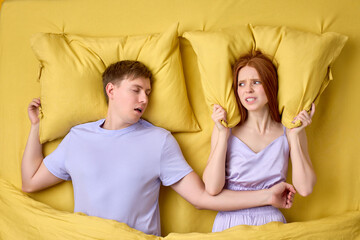 Couple lying in bed, redhead woman is trying to sleep while man is snoring