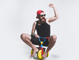 Amazed funny bicycle rider, excited man on colorful bicycle toy in sunglasses, cap. Guy riding...