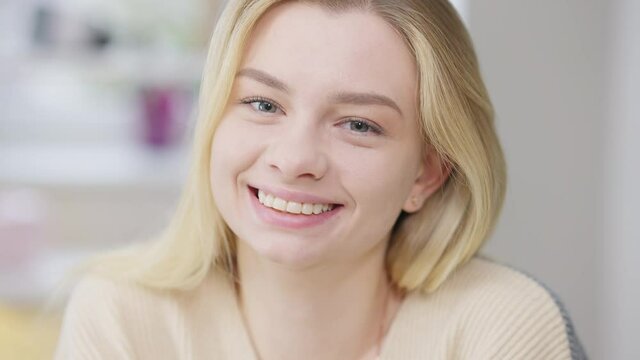 Headshot of cheerful happy beautiful young woman laughing looking at camera. Close-up portrait of joyful positive gorgeous Caucasian blond millennial posing indoors with toothy smile. Joy lifestyle