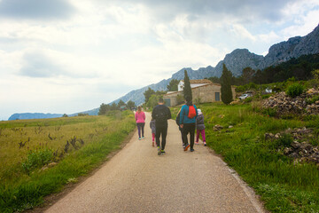 People walking along a path, near the Sierra de Bernia mountains, on a spring day, with cloudy skies.