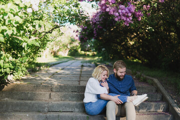Fototapeta premium Romantic and happy caucasian couple in casual clothes hugging on the background of beautiful blooming lilac. Love, relationships, romance, happiness concept. Man and woman walking outdoors together.