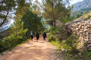 People walking along a path, near the Sierra de Bernia mountains, on a spring day, with cloudy skies.