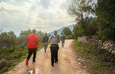 People walking along a path, near the Sierra de Bernia mountains, on a spring day, with cloudy skies.