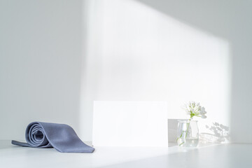 White blank business card mockup. Gray satin tie, white flowers in the sunlight. Elegant wedding...