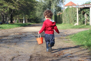 little child playing in the park with a red bucket