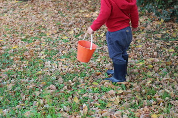 child with boots and a red bucket in autumn