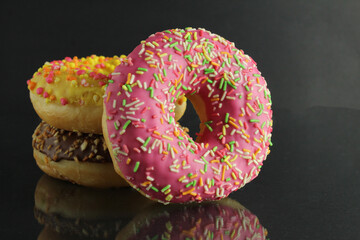 Berliner doughnuts with icing pink yellow lie stops and pink bright stands on a black background with room for text