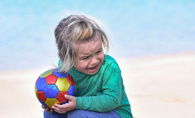 Child baby crying sitting with colorful ball on beach