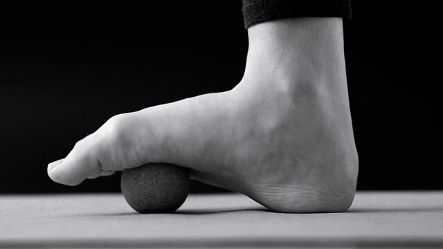 Close up video of foot on cork massage ball for plantar fascia massage and hydration on black background