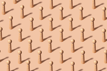 Creative pattern with equal wooden figures representing people on pastel orange background -...