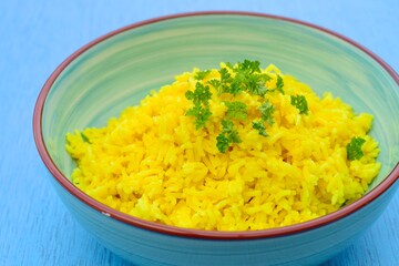 Indonesian yellow turmeric rice or Nasi Kuning in a bowl garnish with chopped parsley. Blue...