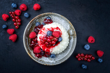 Modern style traditional blancmange almond pudding with wild berry coulis served as top view in a...