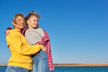 Fototapeta na wymiar Outdoor portrait of happy mom and child daughter hugging together, blue sky background