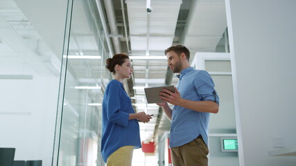 Colleagues looking tablet in modern office. People discussing business indoors.
