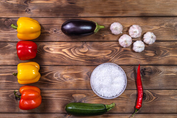 Bell pepper, chili pepper, eggplant, garlic and coarse table salt lie on a brown wooden background.