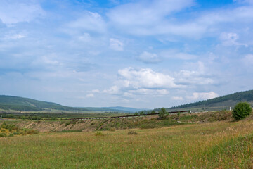 Fototapeta na wymiar Summer mountain landscape of the Cis-Baikal depression. Road Irkutsk - Khuzhir in the foreground. In the distance there are mountains and a Siberian village