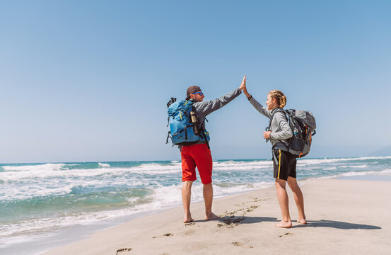 Father and teenager son with backpacks making High FIVE on sandy seaside beach during Lycian Way trekking walk. Famous Likya Yolu Turkish route. Active happy family people vacation concept image.