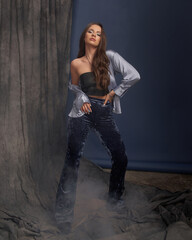 Young beautiful stylish woman in black top, blue pants and jacket with long brunette hair posing...