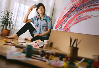 Fototapeta premium Portrait of female artist with paint brush in studio. Creative activity and inspiration concept. Talented people concept.