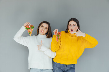 Two female friends holding pizza slices. Young people having fun eating dinner. Isoleted on gray background