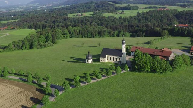 Church of pilgrimage in Wilparting Irschenberg during summer, mountains in background, blue sky, Bavaria Germany, drone view flying downwards

