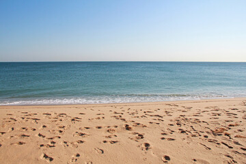 Sandy beach relaxing getaway with foot prints in sand and view of ocean waves, blue sky to relax and meditate