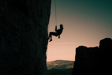 silhouette of woman rappelling held by climbing rope, at sunset in mountain landscape in Etxauri, Navarra, Spain.