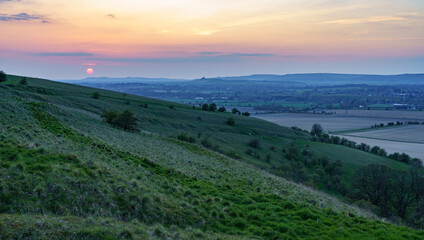 a scenic landscape view across Pewsey and Pewsey Vale with sunset illuminating a colourful evening sky in Wiltshire, North Wessex Downs AONB