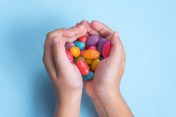 Child's hand holding several Jelly Beans over blue background