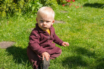 Little boy in overall sitting in grass in a garden looking angry to camera