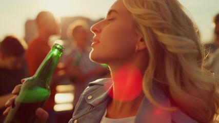 Young woman drinking beer at disco. Smiling girl dancing at sunset roof party.