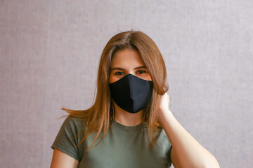 a young brunette girl in a black fabric protective mask looks at the camera and holds her hair with her hand..