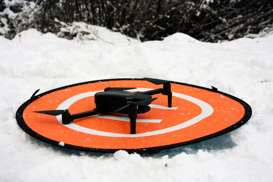 a small drone on its landing base among the cold white snow in the mountains in winter