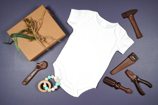 Father's Day or masculine birthday theme baby romper onesie flatlay styled with gift, chocolate tool set and tie. White product mock up with negative copy space for your text or design here.