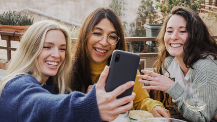 Multiracial girls having fun together in the city while taking selfie with mobile phone - Main focus on hispanic woman face