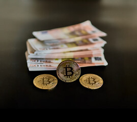 Three Bitcoin coins, along with several 50 euro bills. Concept of power, wealth, economy, Btc, anonymity. Selective focus.